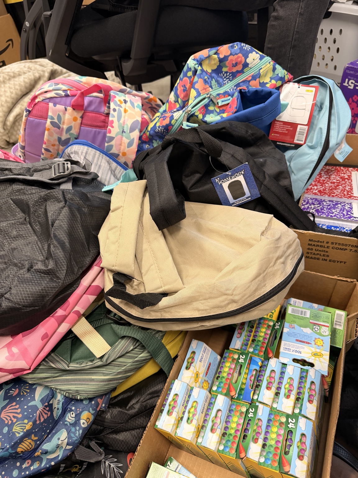 Colorful backpacks, notebooks, and crayons are prepared for a school-supply distribution.